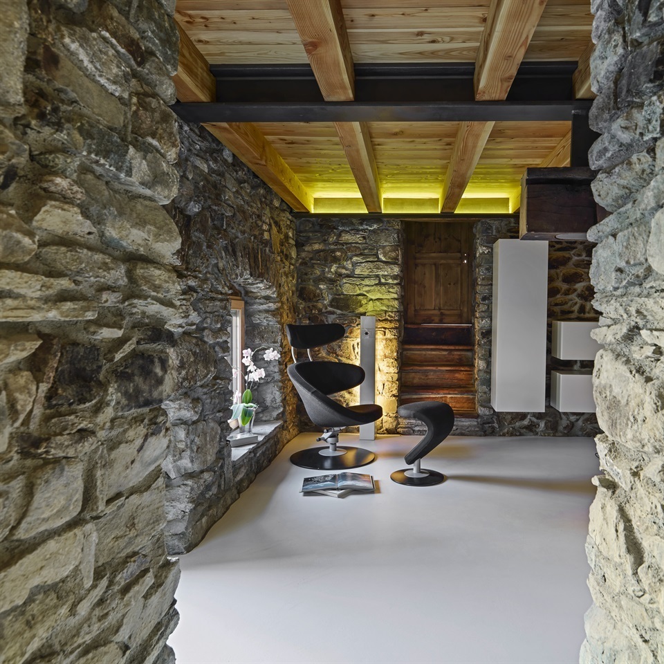 interior shots of a modern living room in the foregorund the leather armcahair the walls are made of stone and the floor is made of resin